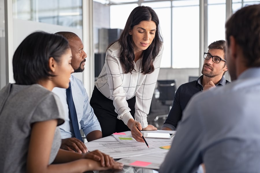 A woman presents something to a boardroom full of executives