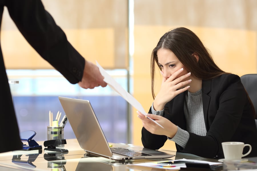 A woman looking shocked at a piece of paper she's being shown in an office setting