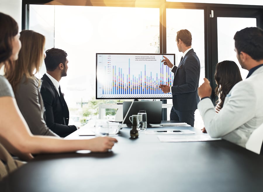 A man presents data to a boardroom of colleagues