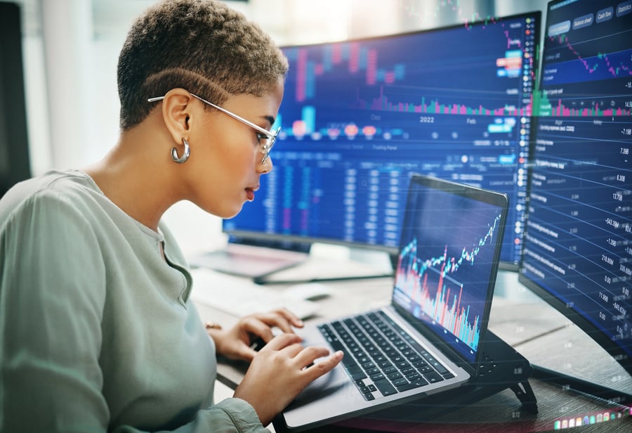 A woman checks on data on a laptop with monitors around her