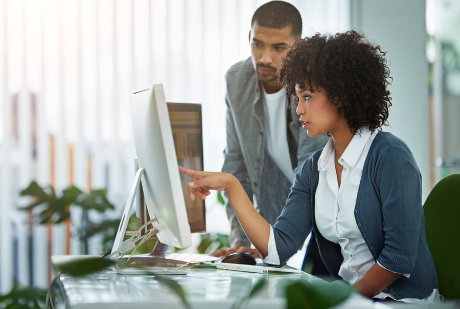 A woman shows a man something on a monitor in an office